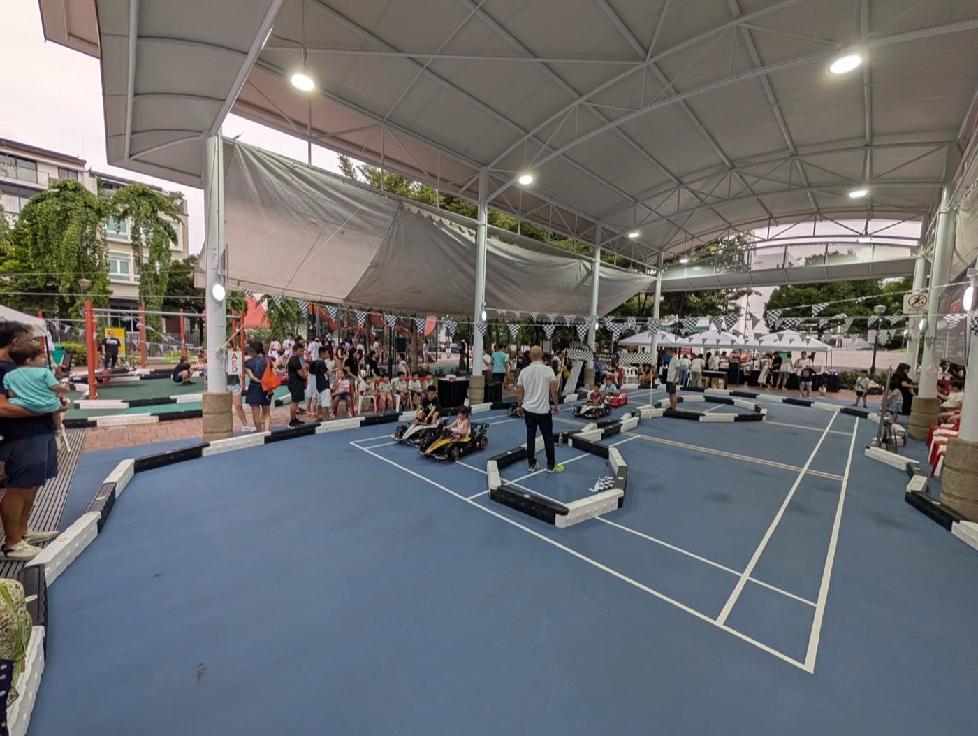 Full circuit built with soft barriers across a sheltered blue sports court, families watching from the sides