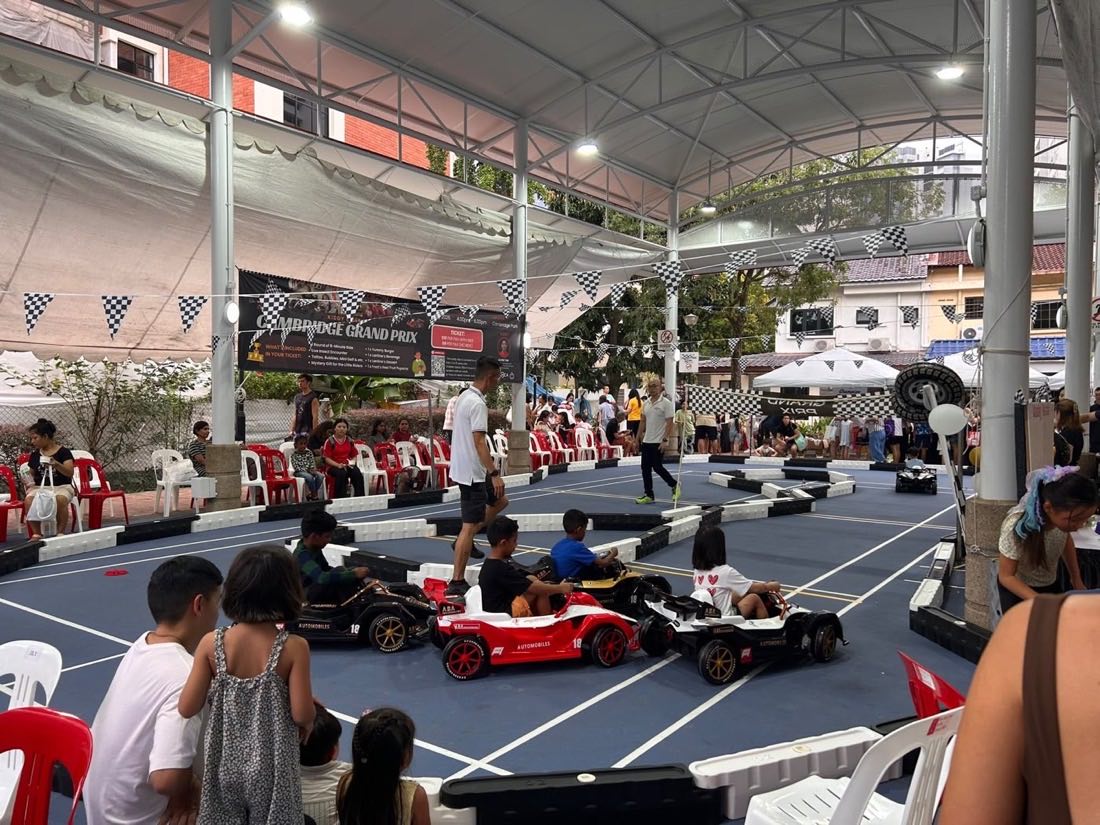 Three ride-on race cars lined up on the grid while crew brief the drivers